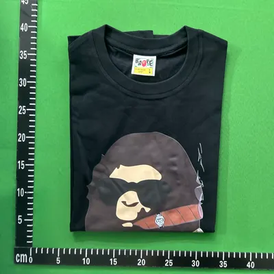 Zdjęcie QC: czarny T-shirt z nadrukiem, złożony na zielonej macie pomiarowej z podziałką centymetrową