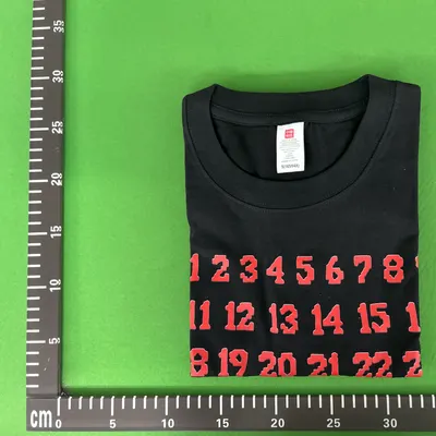 Zdjęcie QC: czarny T-shirt z czerwonym nadrukiem cyfr i widoczną metką wewnętrzną przy kołnierzu
